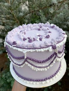 a purple and white cake sitting on top of a table next to some trees in the background