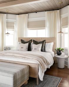 a large bed sitting in a bedroom on top of a wooden floor next to two windows