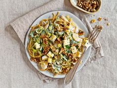 a white plate topped with pasta covered in sauce and toppings next to a bowl of nuts