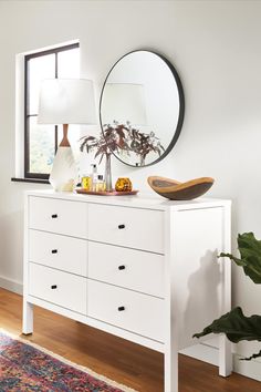 a white dresser topped with a mirror next to a plant