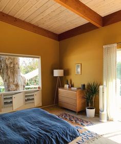 a bedroom with yellow walls and blue bedspread on top of the bed in front of an open window