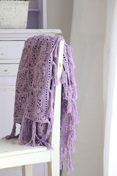 a purple crocheted blanket sitting on top of a white chair