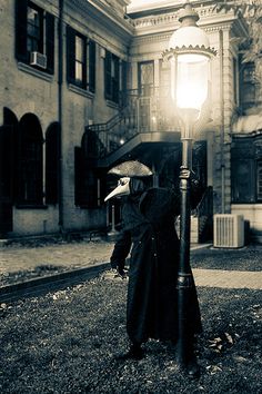 a person dressed in black holding an umbrella next to a lamp post on the grass