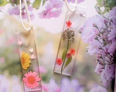 two tags with flowers on them hanging from strings in front of purple and pink flowers