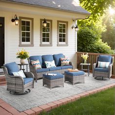 an outdoor patio with blue furniture and pillows on the floor, in front of a white house