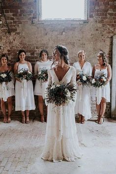 a bride and her bridals standing in front of a brick wall holding bouquets