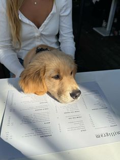 a woman sitting at a table with a dog laying on it's back next to a menu