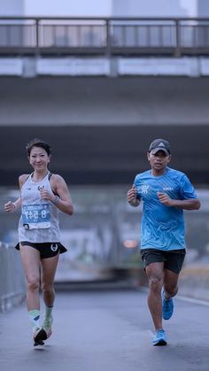 two people running down a street next to a bridge