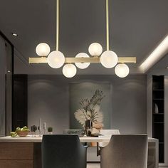 a dining room table with chairs and lights hanging from it's ceiling in front of a kitchen