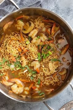 a pot filled with noodles and shrimp on top of a table next to utensils