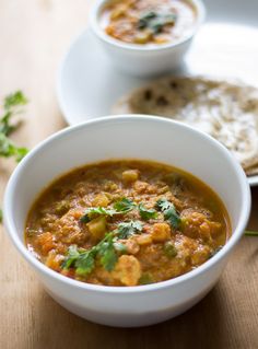 two bowls of soup on a table with pita bread and garnishes