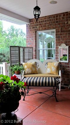 a porch with two chairs and a couch on top of it next to potted plants