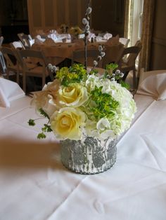 a centerpiece with white and yellow flowers on a table in a banquet hall setting