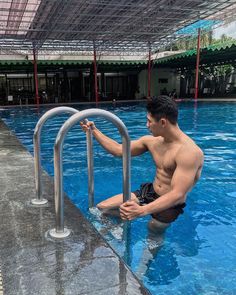 a man sitting on the edge of a swimming pool next to a metal hand rail