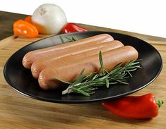 two hot dogs on a black plate next to some peppers and garlic, along with an orange pepper