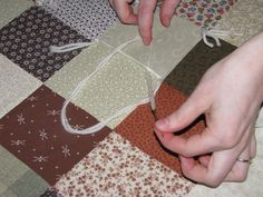 two hands are stringing fabric together on a quilted tablecloth with various patterns and colors