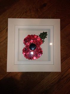 a white frame with a red and pink wreath in it on top of a wooden floor