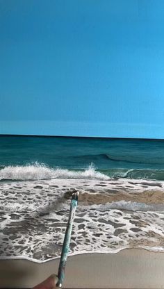 a person is holding a paintbrush in front of the ocean