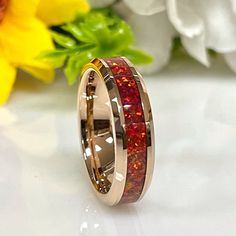 a wedding ring with red and gold inlays sits on a table next to flowers