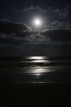 the full moon shines brightly over the ocean on a cloudy night with dark clouds