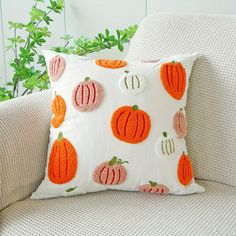 an orange and white pumpkin pillow sitting on top of a couch next to a potted plant