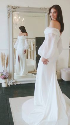 a woman is standing in front of a mirror wearing a white dress and posing for the camera