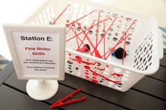 a white basket sitting on top of a table filled with red and black pins next to a sign stating fine motor skills