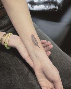 a woman's hand with a small feather tattoo on her left wrist and the other arm