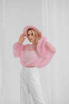 a woman in white pants and pink sweater posing for the camera with her hands on her head