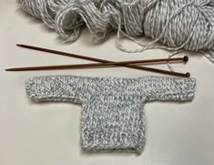 two skeins of yarn and knitting needles on a white surface with gray knitted sweater