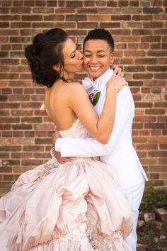 a man and woman in formal wear embracing each other outside with brick wall behind them