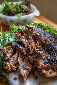 some meat and greens on a cutting board with a bowl of salad in the background