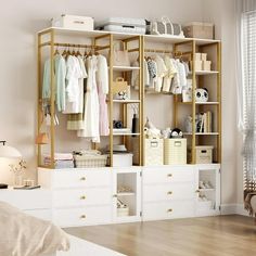 a white and gold closet with lots of clothes hanging on the shelves next to a bed