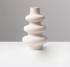 a white vase sitting on top of a table next to a gray wall in the background