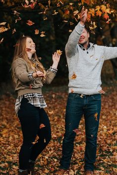 a man and woman are throwing leaves in the air while standing under a tree with their hands up