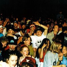 a large group of people standing around each other at a concert, some with their hands up in the air