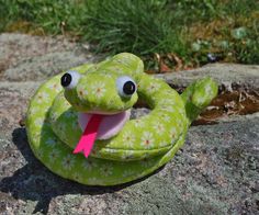 a green stuffed animal with a pink ribbon in its mouth sitting on top of a rock