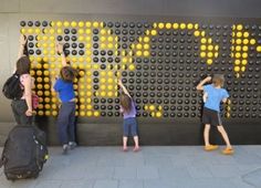 three children are standing in front of a wall made out of yellow and black circles