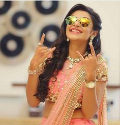 a woman in a pink sari and gold jewelry is making the peace sign with her hands