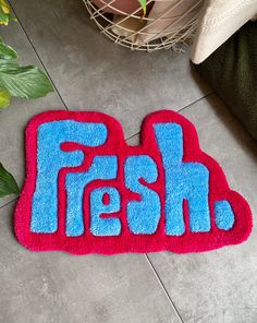 a red and blue rug with the word fresh on it sitting next to a potted plant