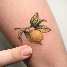 a person with a tattoo on their arm holding up a small piece of fruit and leaves