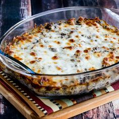 a casserole dish with cheese and meat in it sitting on a wooden tray