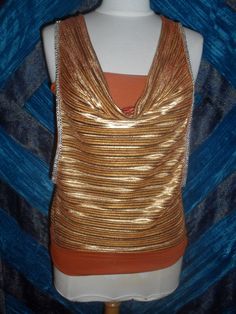 Unusual and glitzy!  Gold pleated draped neck blouson over orange stretch tank top with straps.  Rhinestone braid trim on armholes.  Back is slashed (see photo 2) and tied at neck.  There is a band of the stretch material at the hem which can be pulled down on the hips or worn on the waist for a more bloused effect.  Deep armholes to reveal the tank top. Made in France. Washable. No size or maker's labels. 92% Polyester 8% Elastane Measured flat  in inches Bust (stretched)  17ins (Tank top part) Orange Sleeveless Tops For Party, Orange Sleeveless Top For Night Out, Sleeveless Orange Party Tops, Orange Stretch Tank Top For Party, Stretch Orange Tank Top For Party, Gold And Orange, Pleated Drapes, Stretch Band, Rhinestone Trim