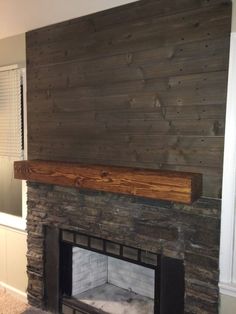 a stone fireplace with a wooden mantle in the middle and white paint on the walls