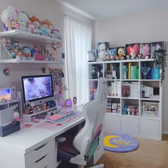 a white desk topped with a computer monitor next to a window filled with lots of toys