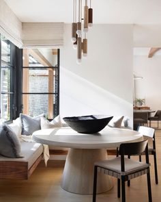 a dining room table with chairs and a bowl on top of it in front of a window