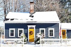 a blue house covered in snow with wreaths on the front door and yellow door