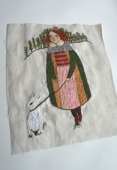 an embroidered piece of cloth with a woman and dog on it's side, in front of a white background