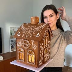 a woman holding up a large gingerbread house