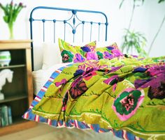 a bed with green and pink bedspread next to a book shelf